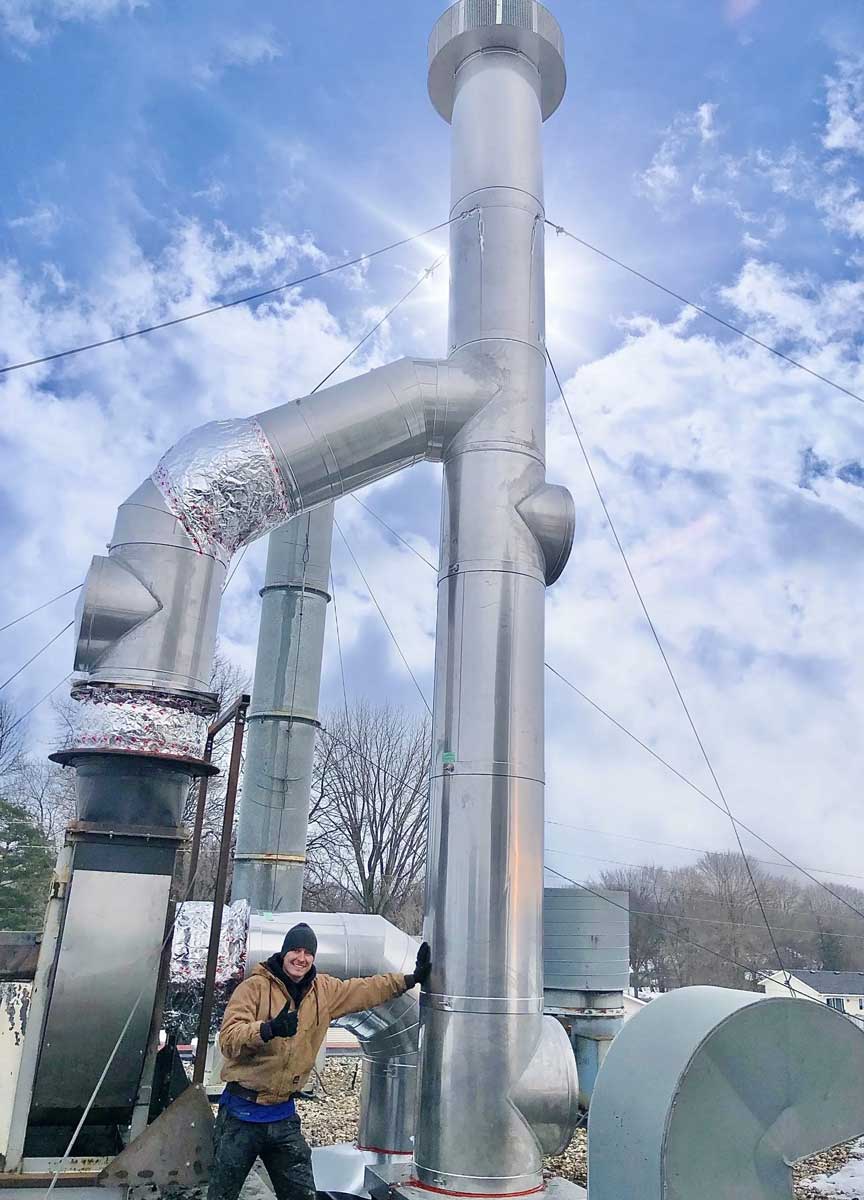 Worker beside large industrial ventilation duct and chimney