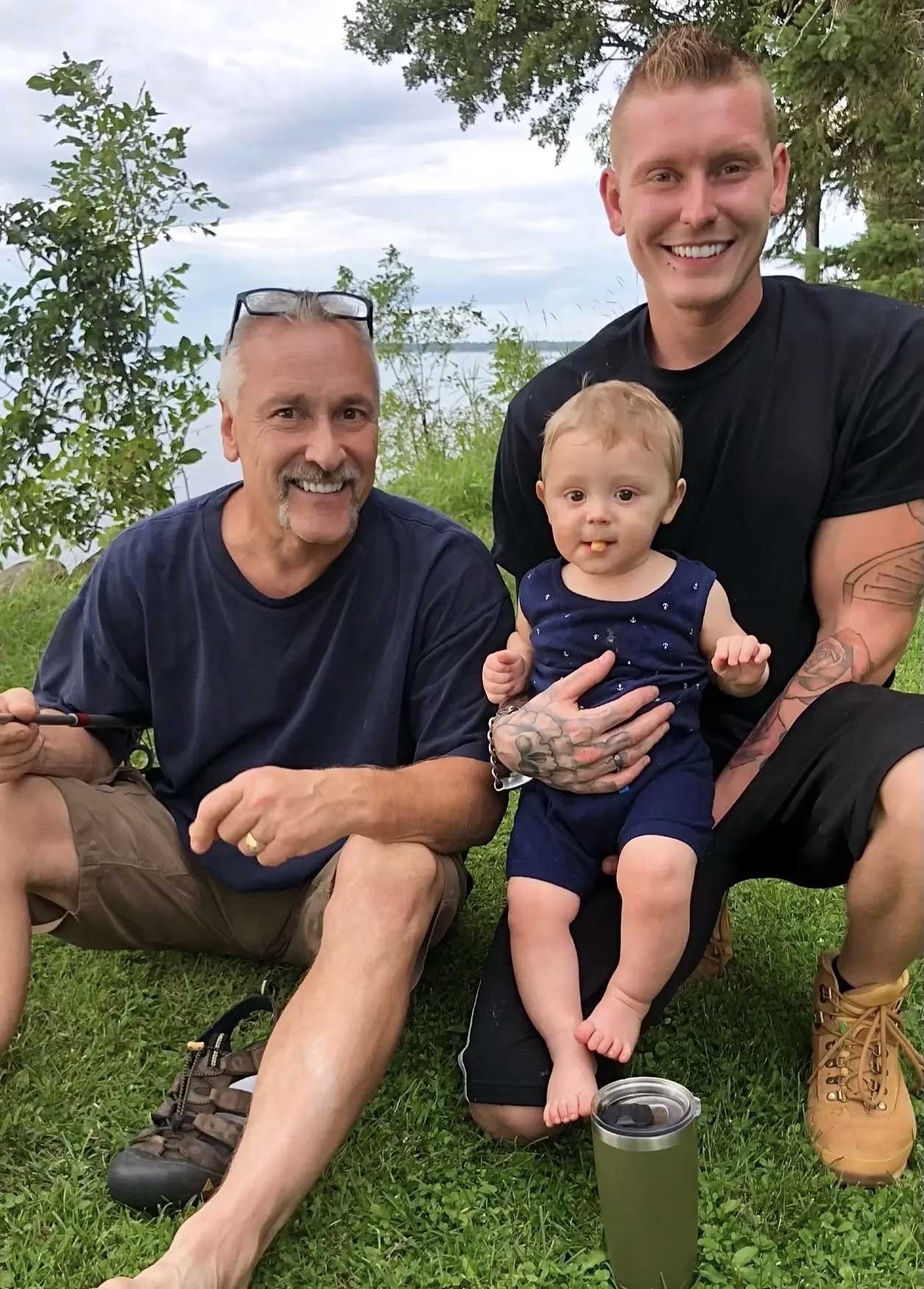 Two men and baby smiling by lakeside