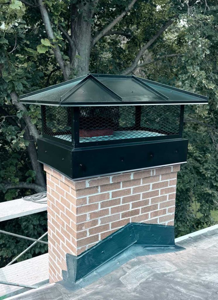 Custom black metal chimney cap installed on a brick chimney